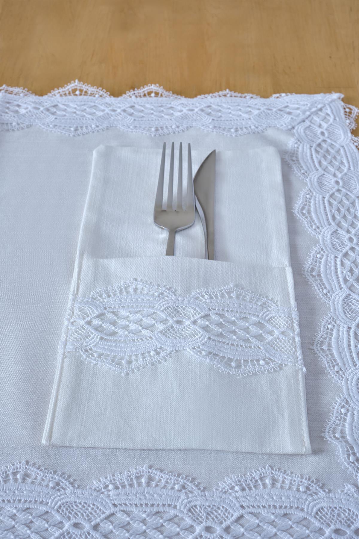 Portatovaglioli in tessuto bianco con ricami in pizzo, con forchetta e coltello su un tavolo