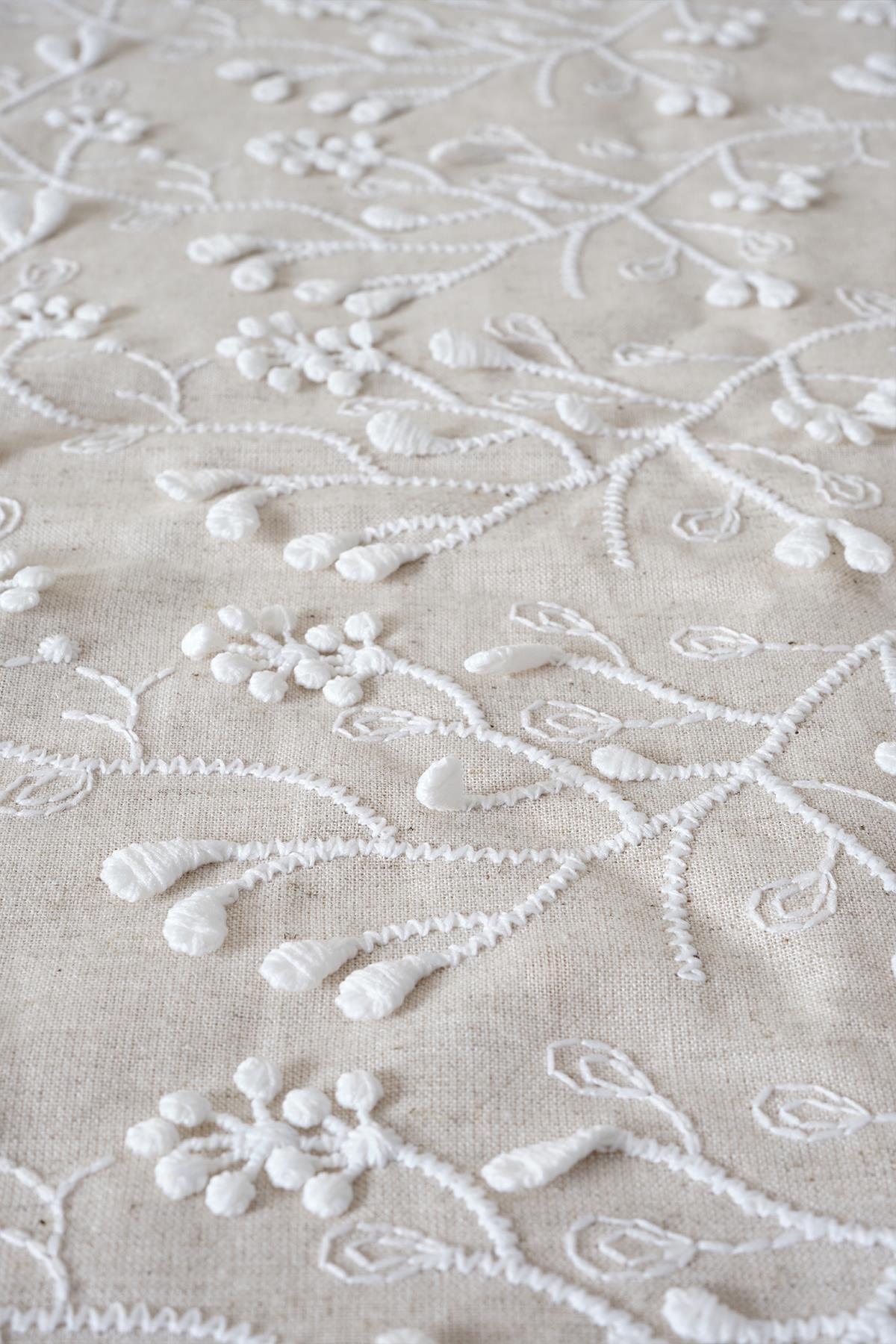 Dettaglio di un tessuto ricamato con motivo floreale bianco in rilievo su fondo beige