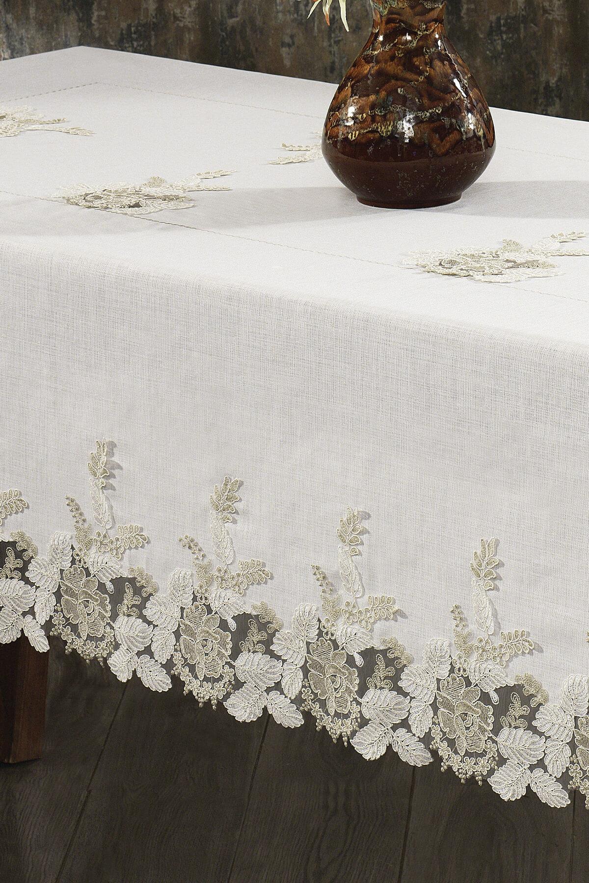 Tovaglia color crema in pizzo, antimacchia, accanto a un tavolo elegante e un vaso in ceramica.