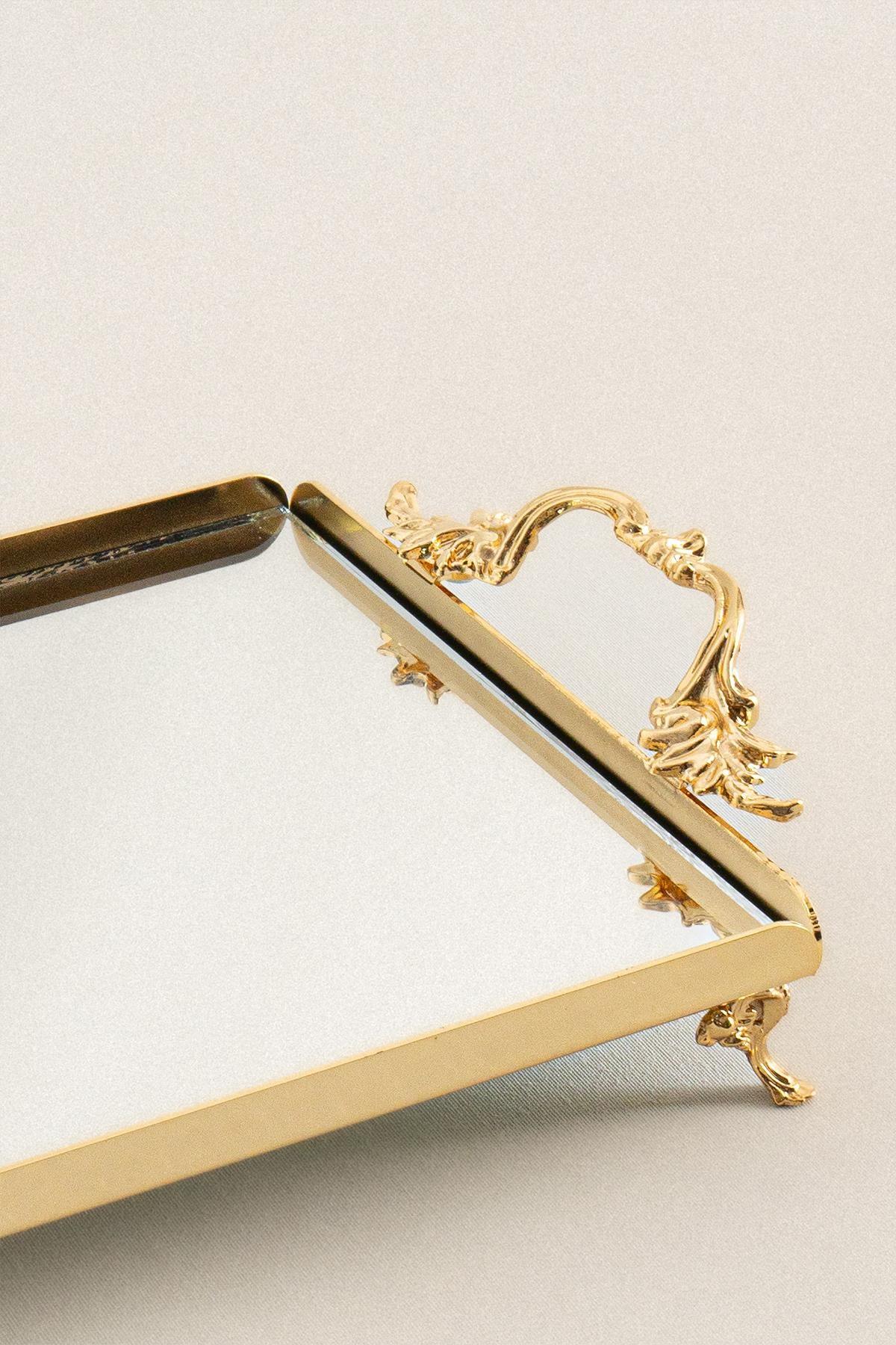 Piccolo vassoio dorato con manici eleganti, base decorativa e superficie a specchio rettangolare.