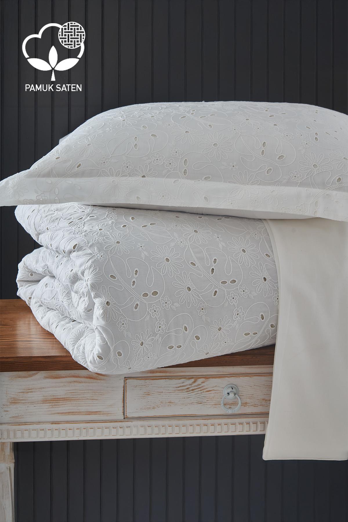 Set di biancheria da letto matrimoniale in raso di cotone bianco con ricami, piegato su un tavolo.