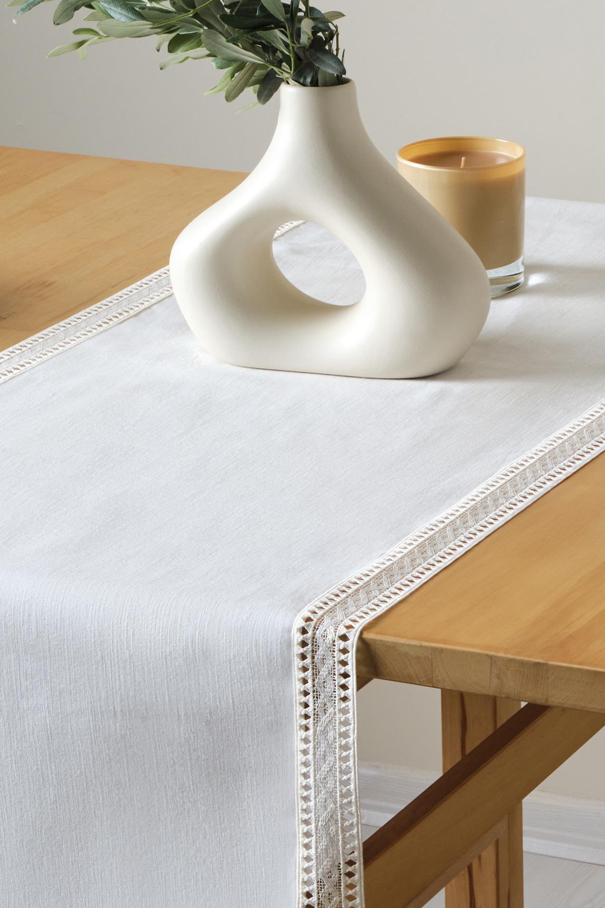 Runner bianco in pizzo, presentazione decorativa con vaso moderno e candela su tavolo in legno