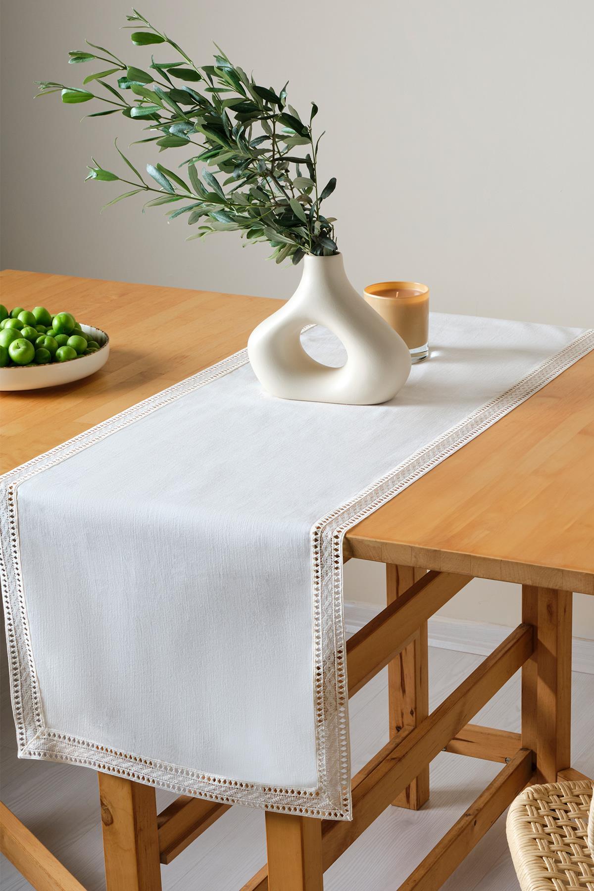 Runner bianco in pizzo su tavolo in legno, con vaso moderno e piatto di frutta verde