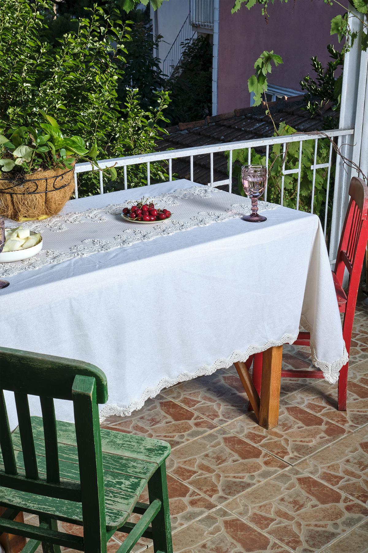 Tavolo da balcone con tovaglia bianca con dettagli in pizzo, affiancato da sedie rosse e verdi