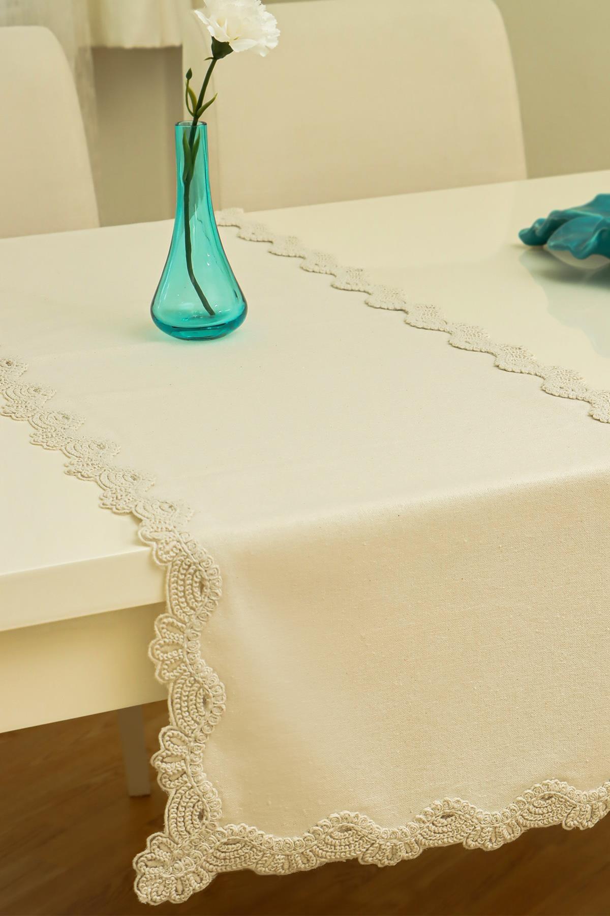 Runner da tavola color crema con dettagli in pizzo, su un moderno tavolo da pranzo con vaso decorativo