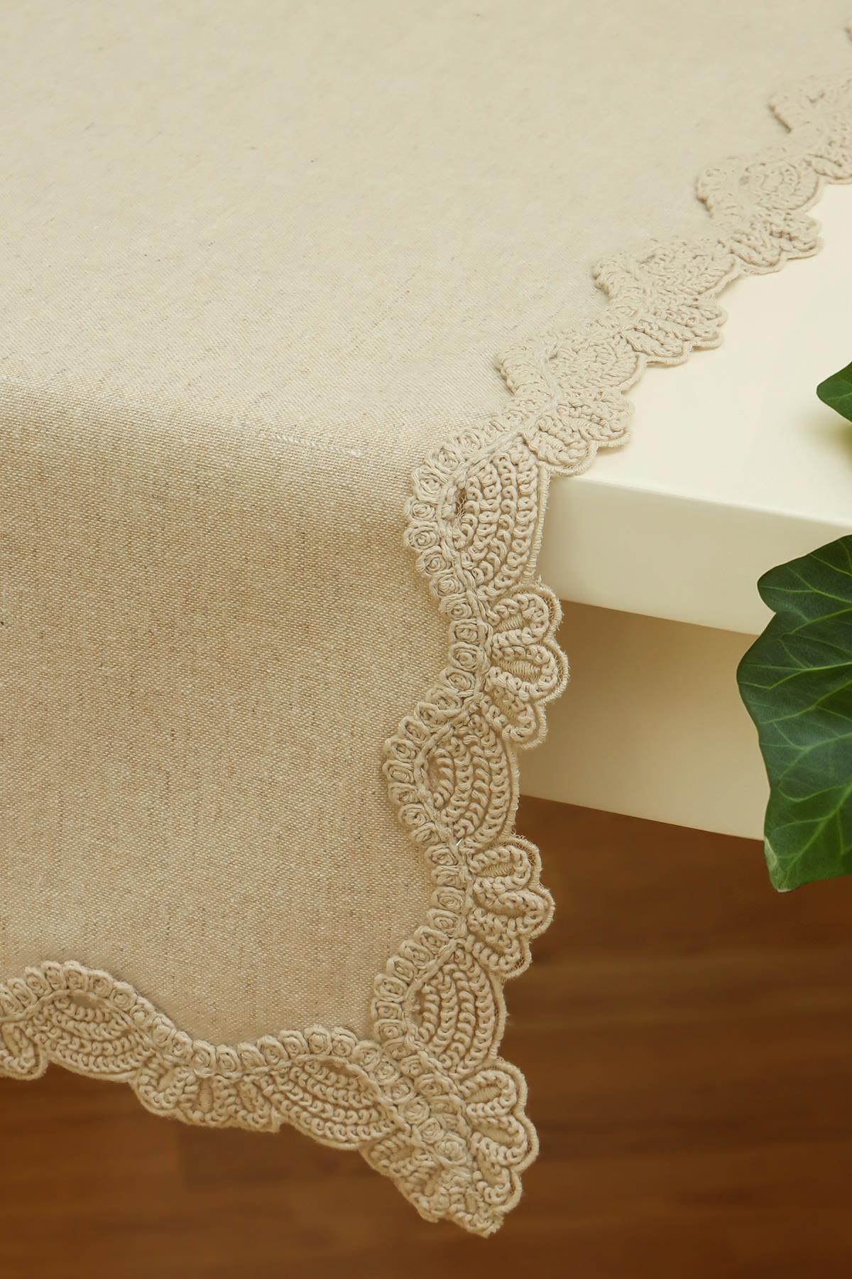 Tovaglia color crema con bordo in pizzo, su un tavolo rettangolare