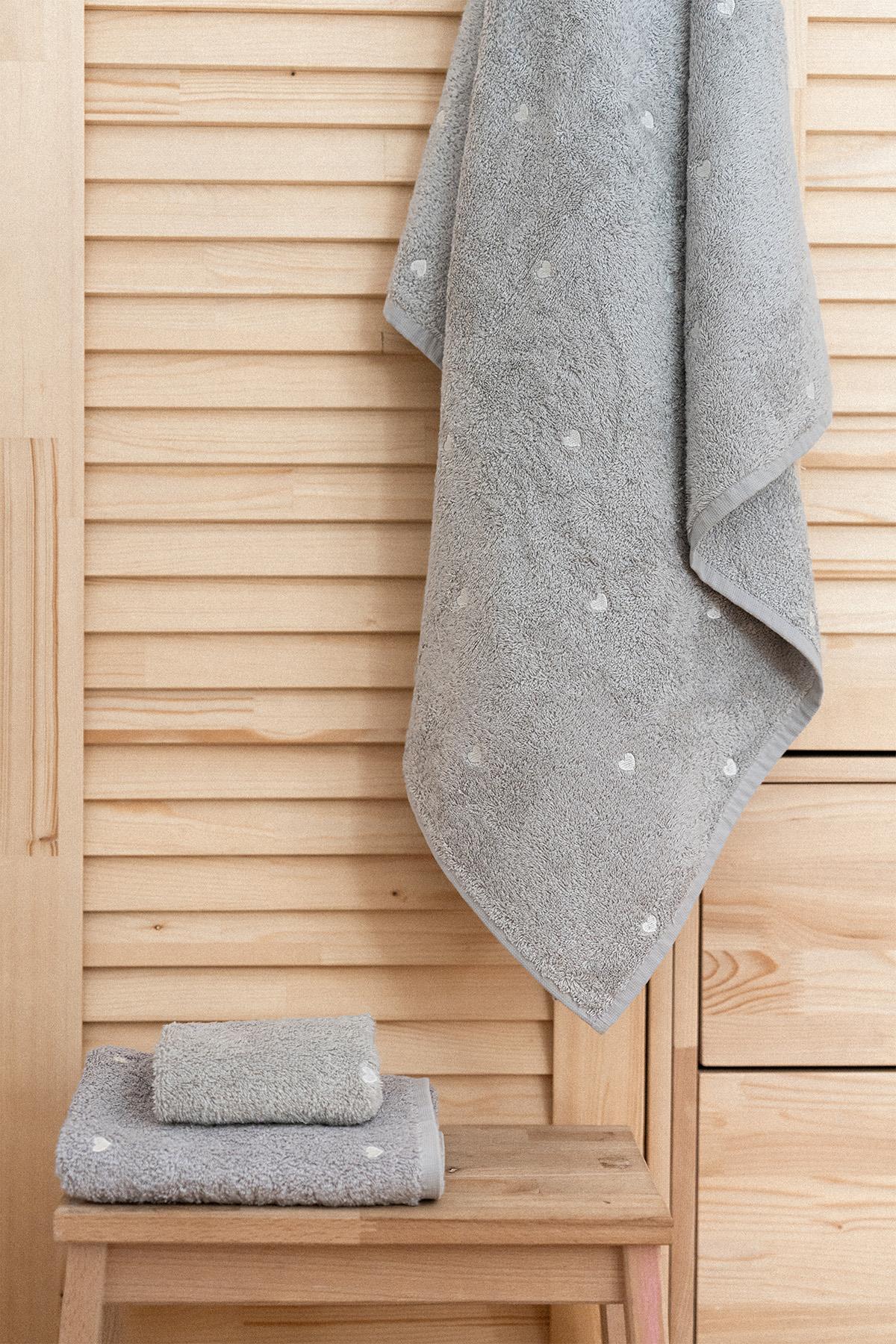 Asciugamano da bagno grigio di qualità con motivo a cuori bianchi, esposto su un pavimento in legno