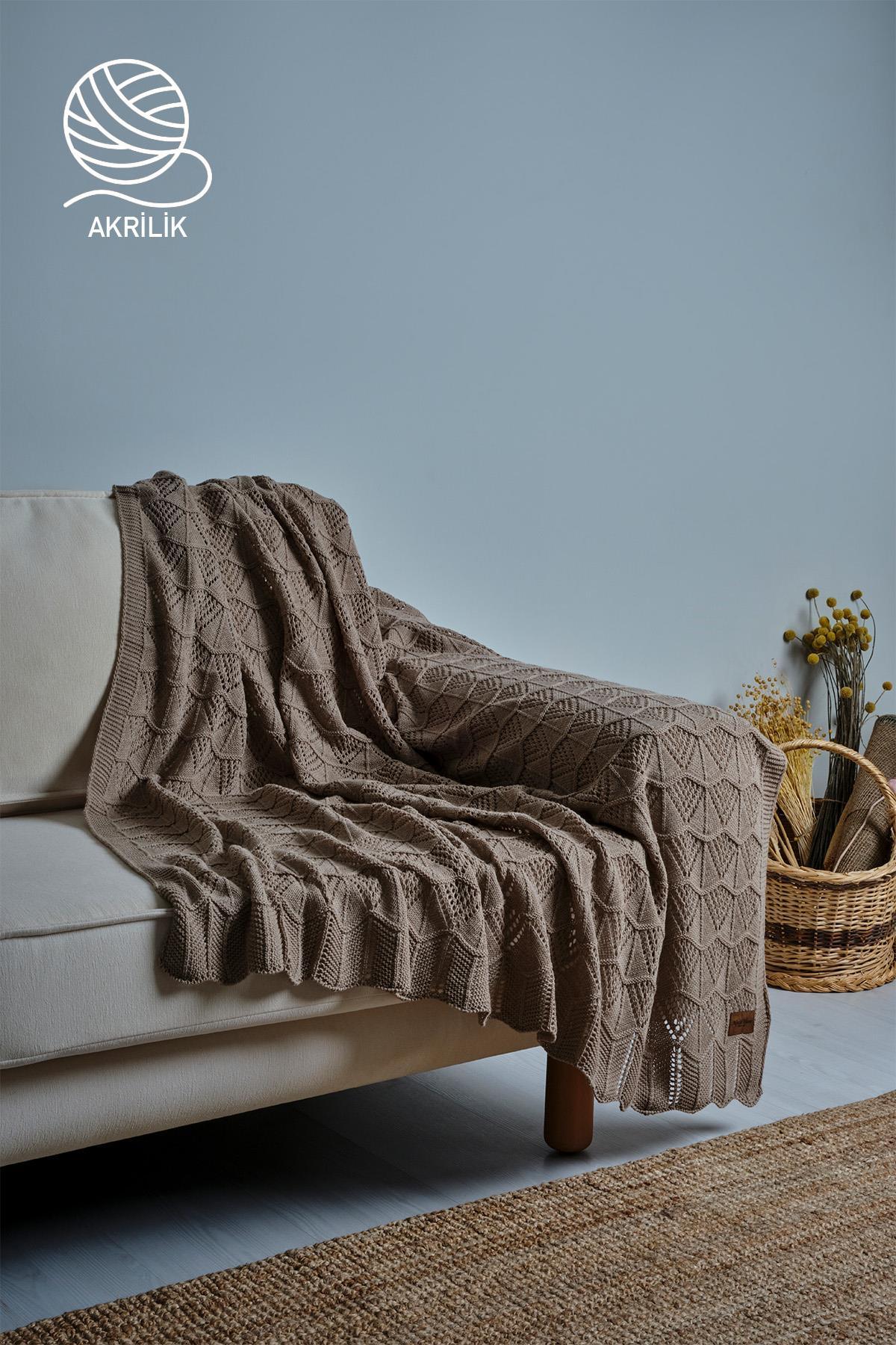 Coperta da TV in maglia grossa acrilica marrone stesa su un divano color crema, ambiente decorativo