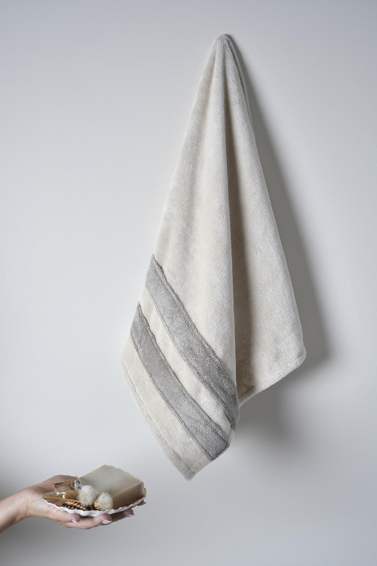 Accappatoio in cotone beige appeso alla parete, con sapone artigianale e accessori da bagno.