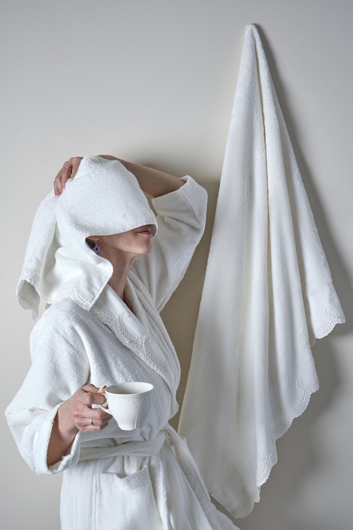 Donna con accappatoio in bambù bianco che tiene in mano una tazza, con un asciugamano appeso alla parete