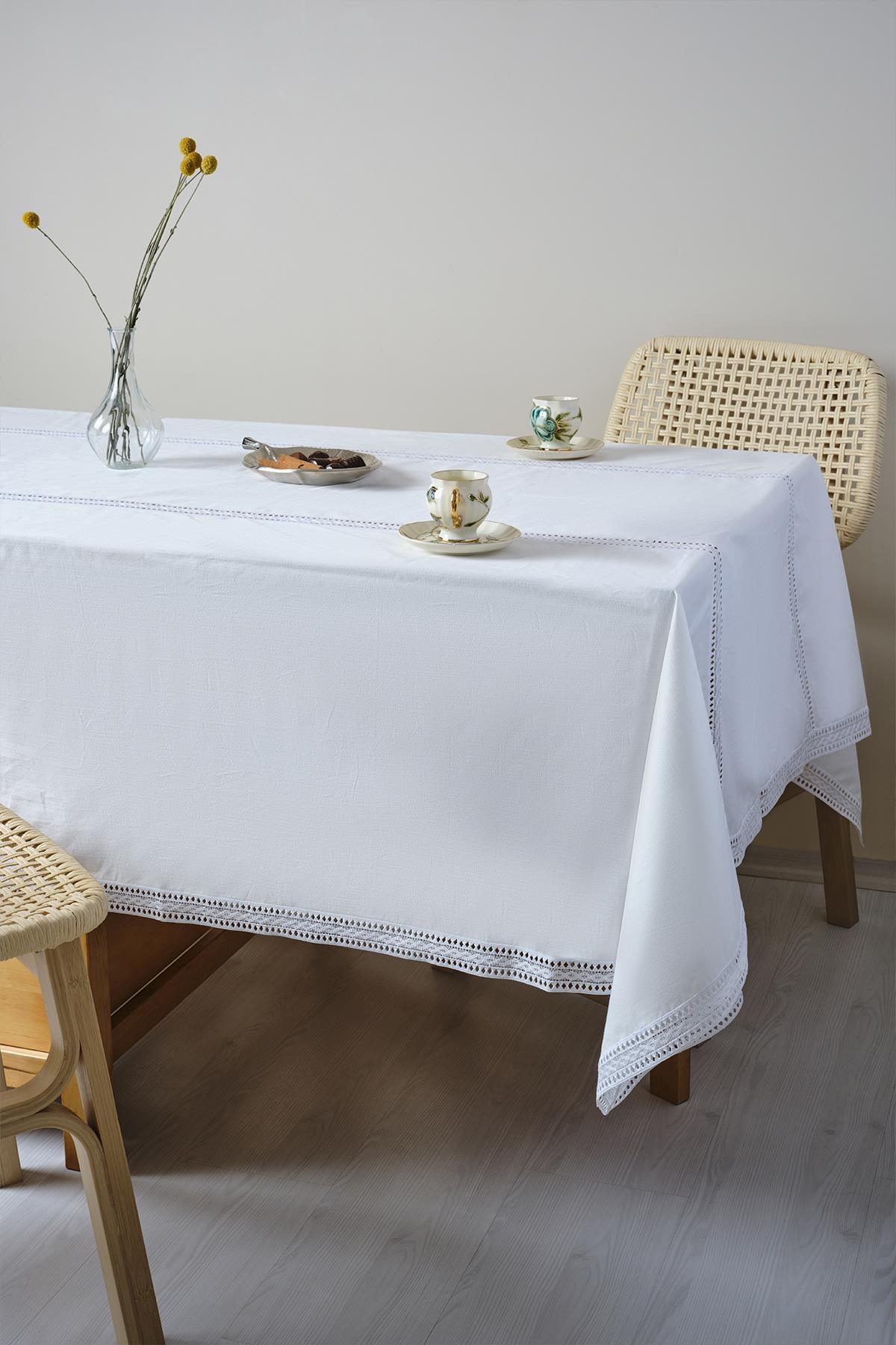 Tavolo coperto da una tovaglia bianca, con tazze in porcellana e un vaso di fiori sopra.