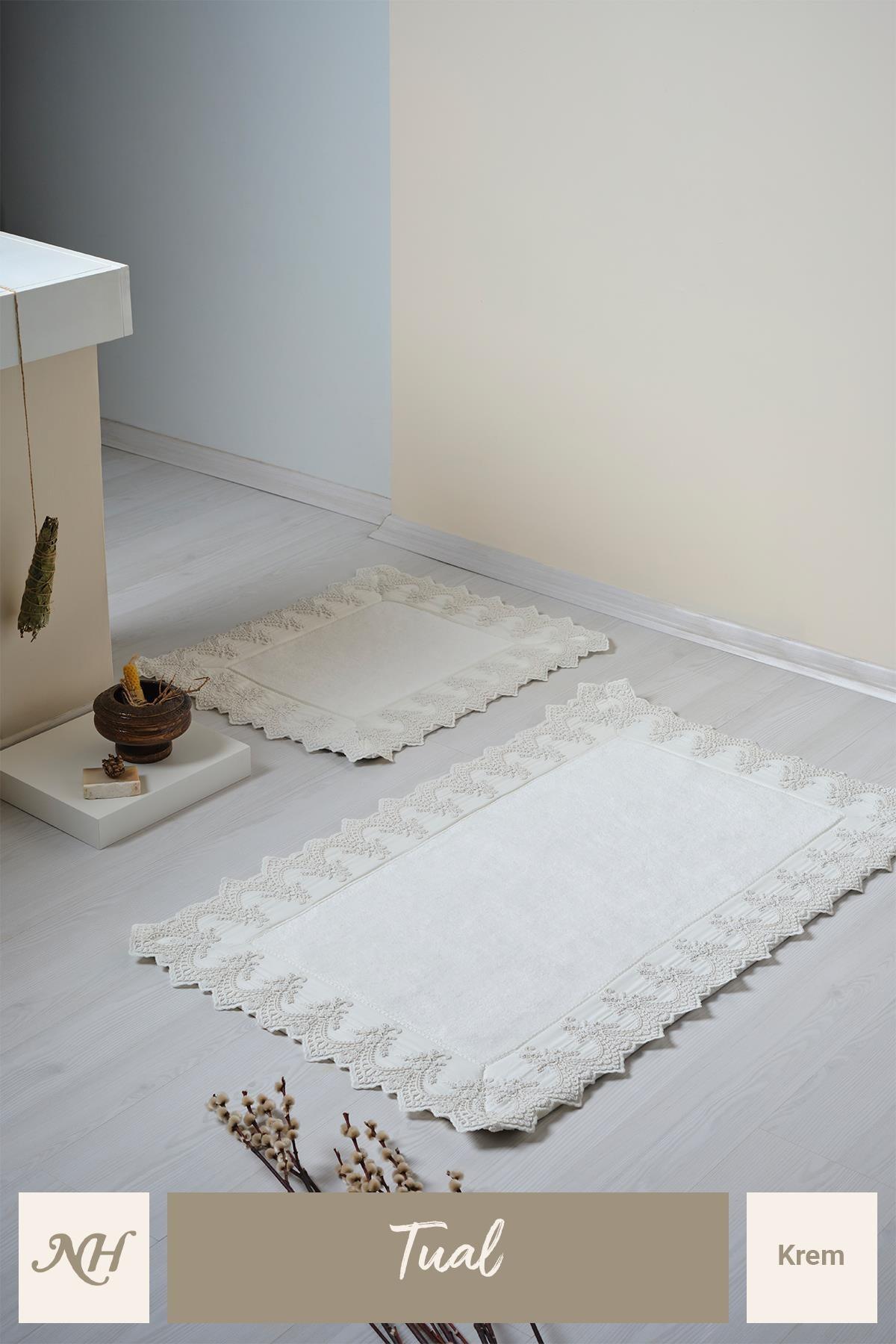 Set di due tappetini color crema con ricami in pizzo, posizionati su un pavimento del bagno moderno ed elegante