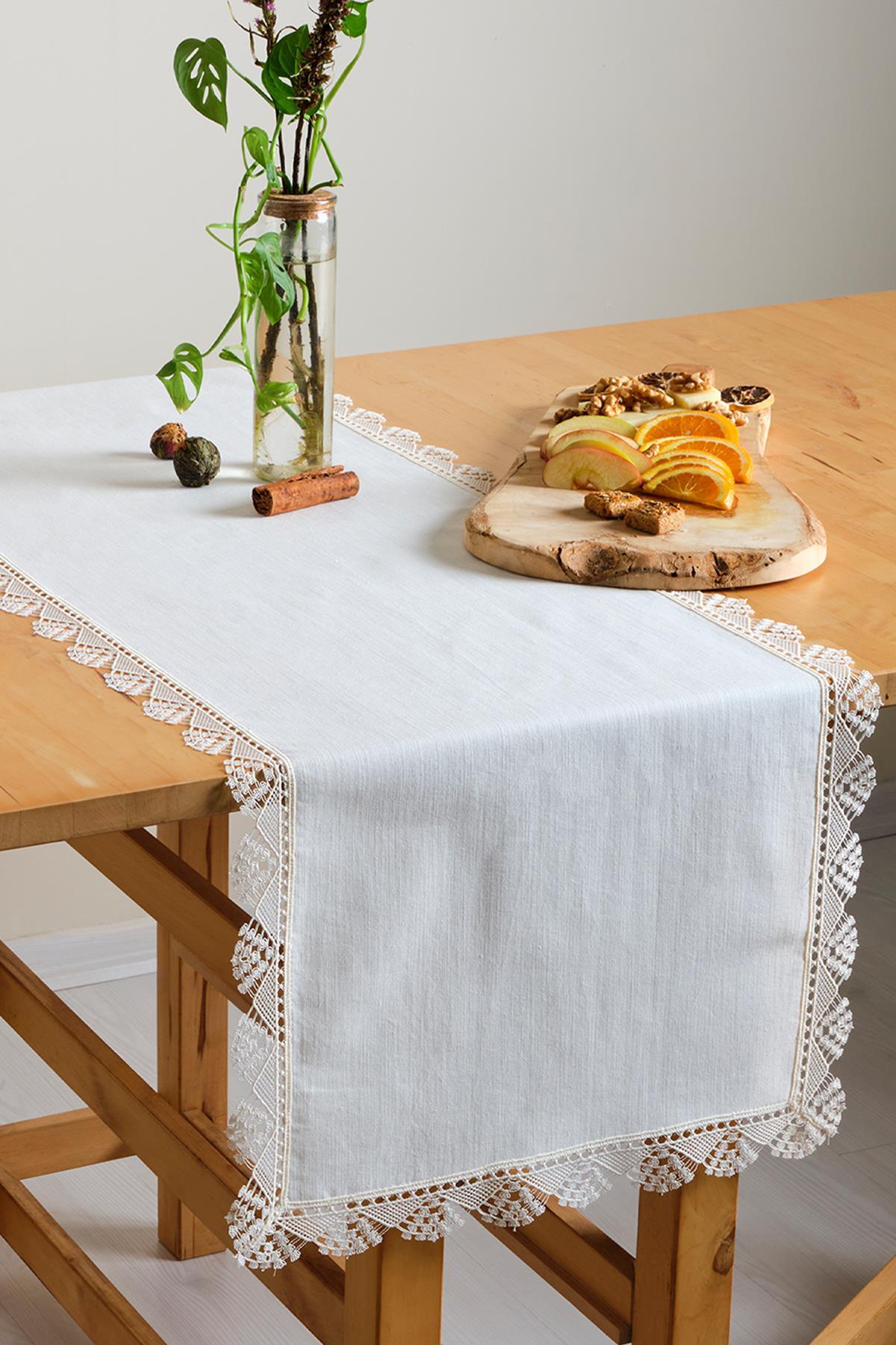 Runner bianco in pizzo, tovaglia decorata con frutta e pianta ornamentale su tavolo in legno