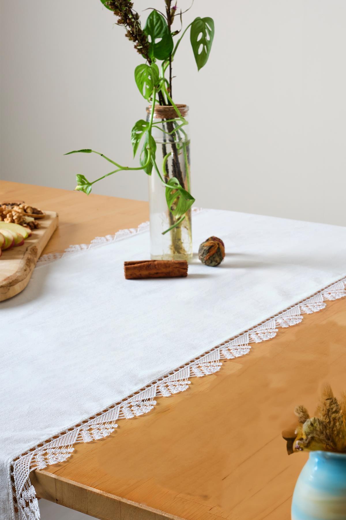 Runner da tavola bianco in pizzo, dall'aspetto decorativo elegante e raffinato su un tavolo in legno.